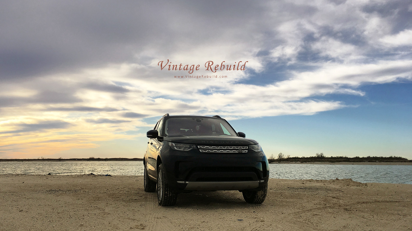 Black 2017 Land Rover Discovery HSE Luxury SUV offroad driving on beach sand at sunset, Jetty Park, Matagorda, Texas.