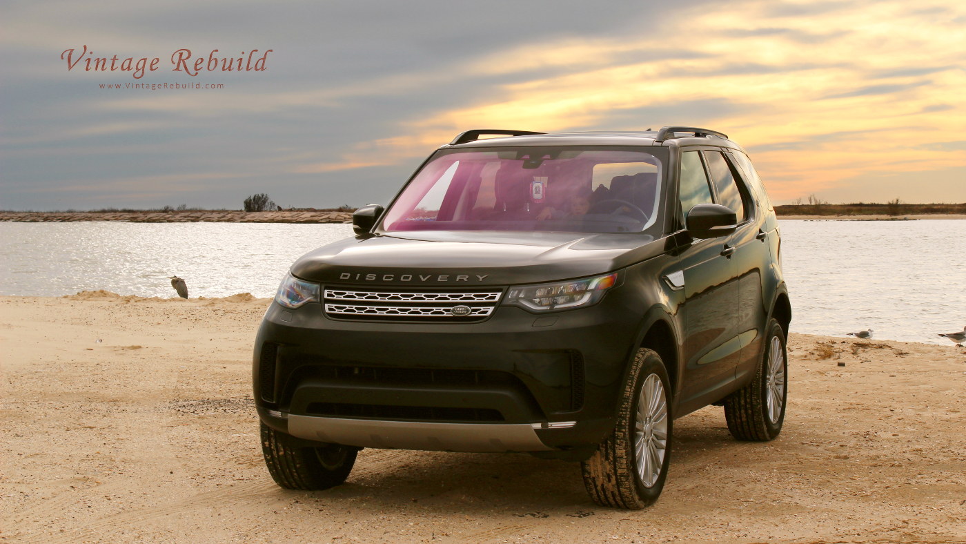 Black 2017 Land Rover Discovery HSE driving on sand offroading at beach during sunset.